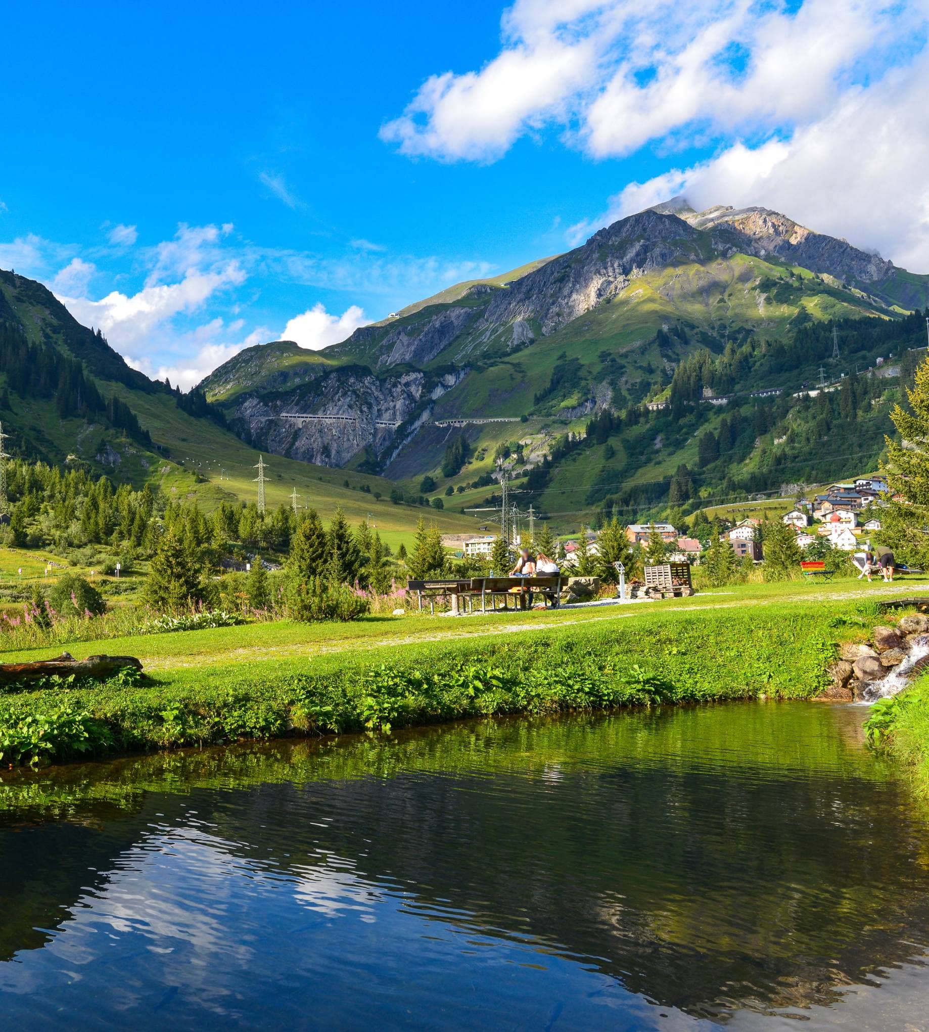 Luxury mountain living in the Austrian Alps: A summer view of a valley pond and village near Lech am Arlberg.