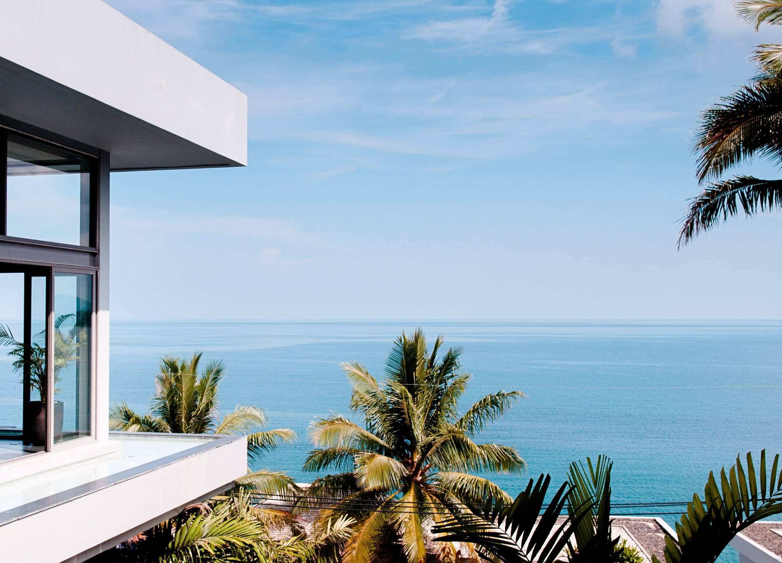 Large infinity pool with turquoise water in which a man on the edge contemplates the view of hedges and trees.  At the edge of the pool are bright folded umbrellas.