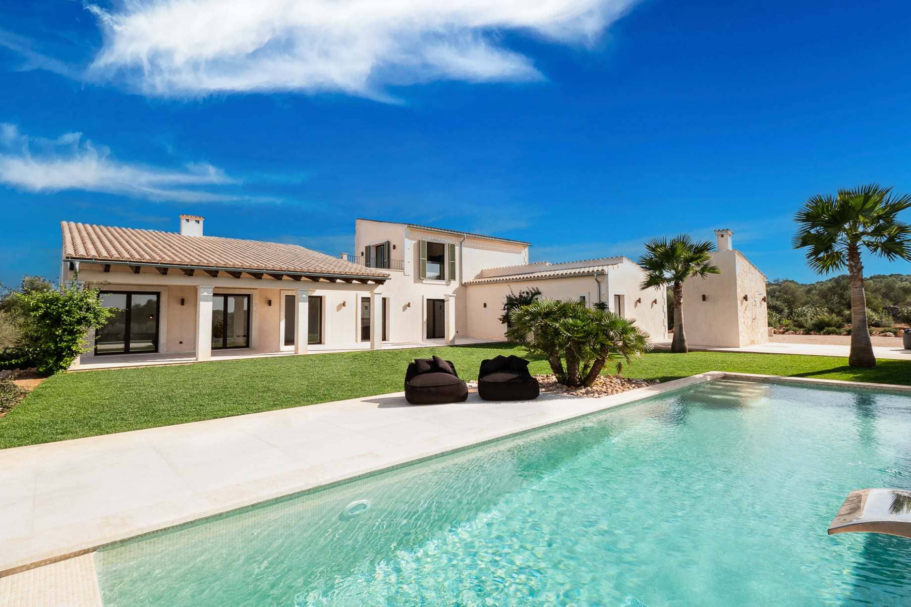 Luxe vastgoed op Mallorca: Een moderne mediterrane finca met een groot zwembad, groen gazon en palmbomen.