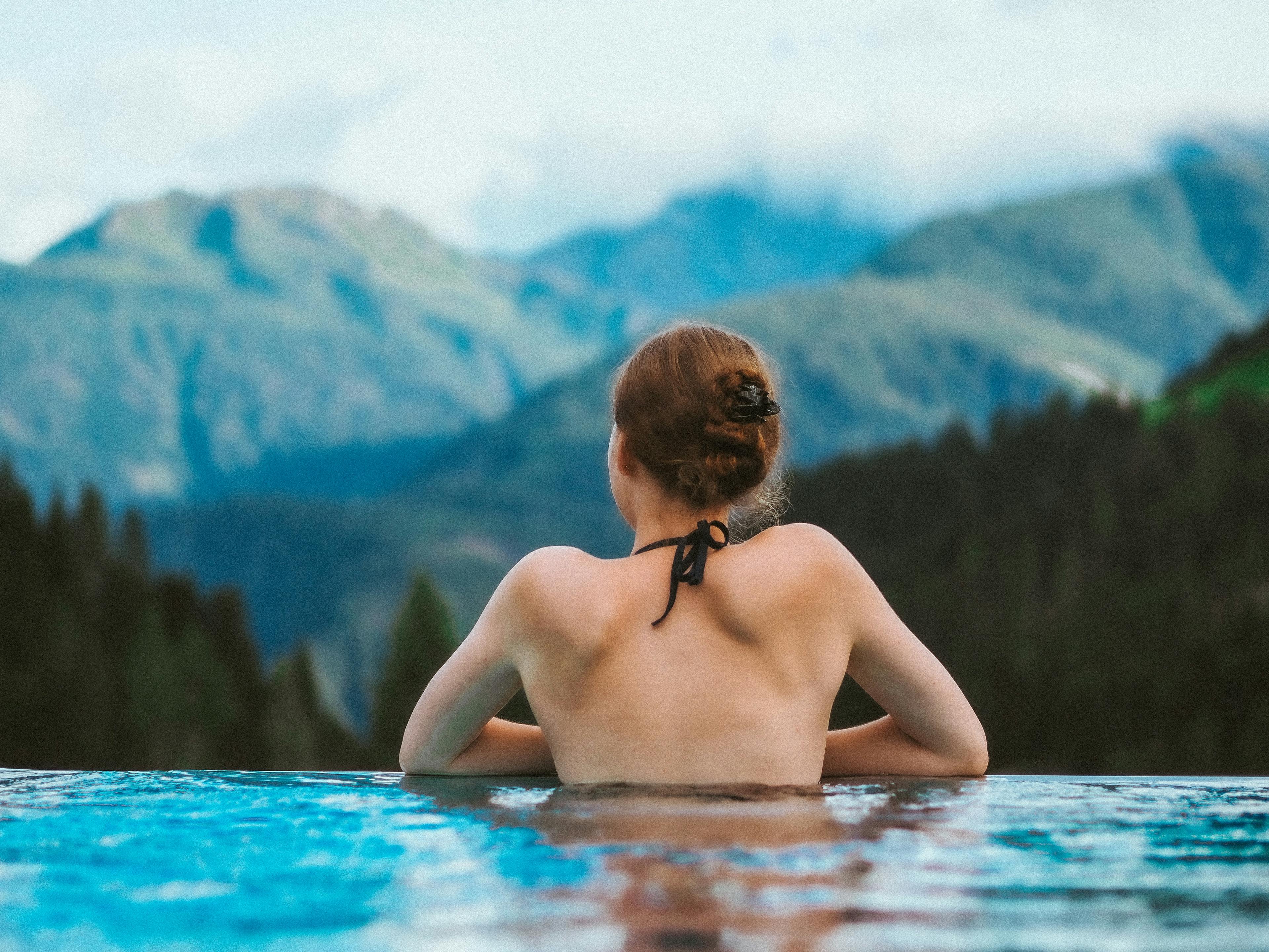 Junge Frau mit braunen Haaren liegt im Infinity Pool, Ausblick auf die Berge