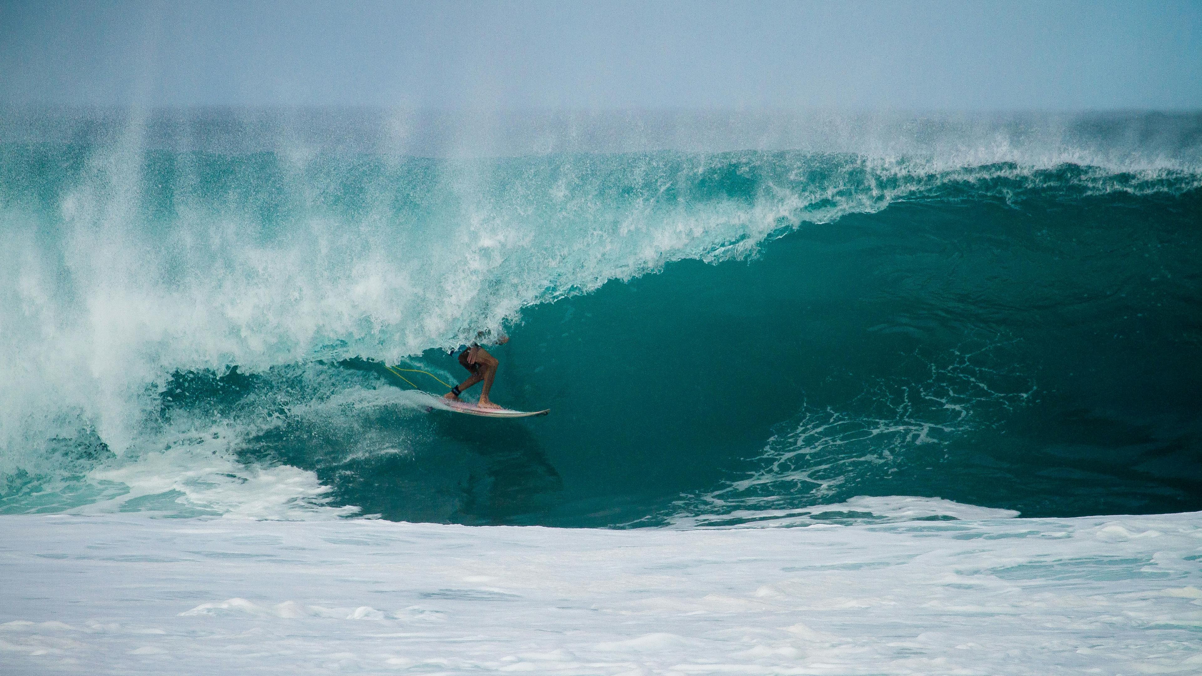 türkisfarbendes Wasser, welches sich gerade zu einer hohen Welle formt.Mittendrin erkennt man einen Surfer.